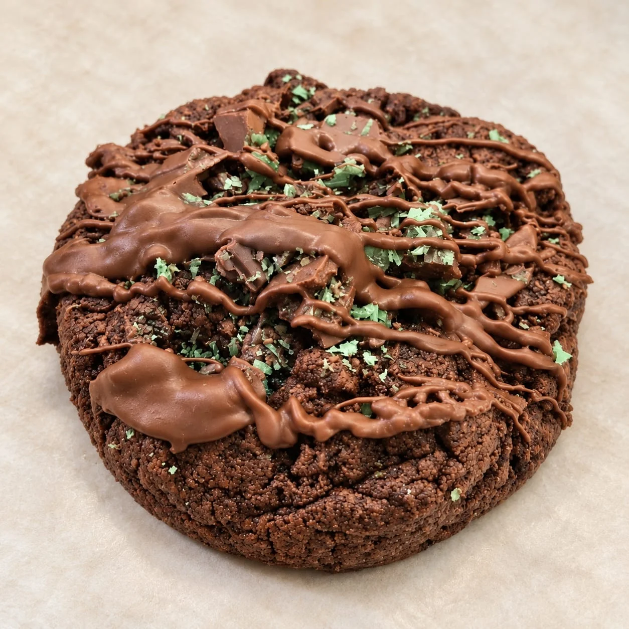 A chocolate cookie topped with a chocolate drizzle and green Peppermint Crisp pieces